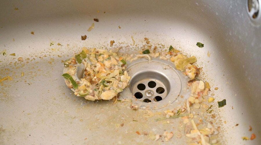 Close up on dirty clogging kitchen sink drain. Blur and selective focus of sink hole clogging up with food particles